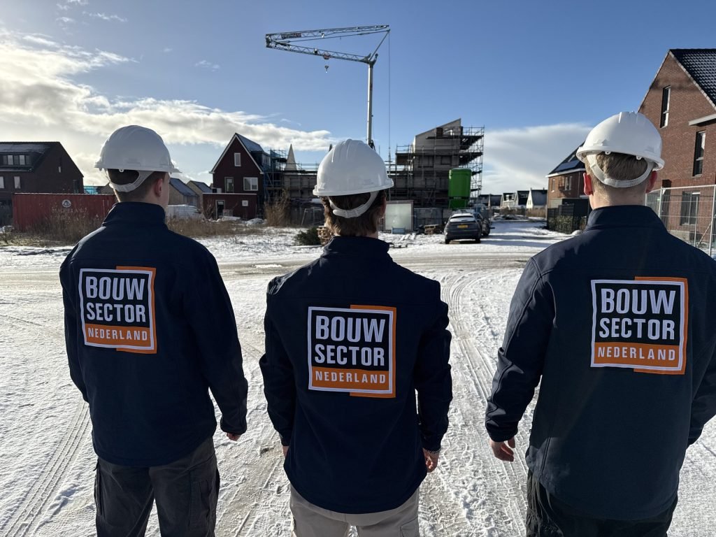 Drie vakmensen van Bouwsector Nederland met witte helm en logo op de rug bij nieuwbouwwoningen